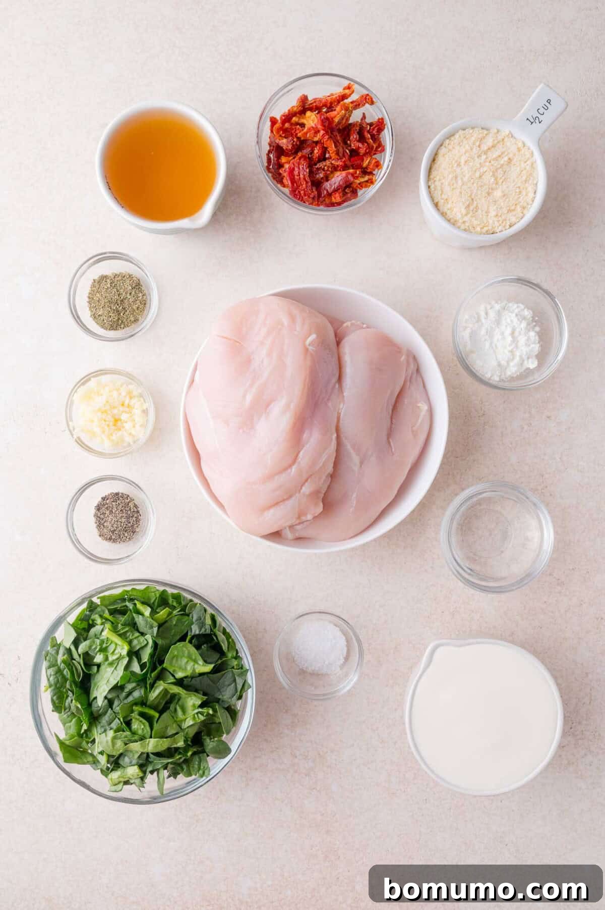 Creamy Tuscan Chicken in the Slow Cooker 4 Top-down view of chicken breasts, fresh spinach, cream, sun-dried tomatoes, parmesan cheese, garlic, salt, pepper, Italian seasoning, and cornstarch in individual bowls on a countertop.