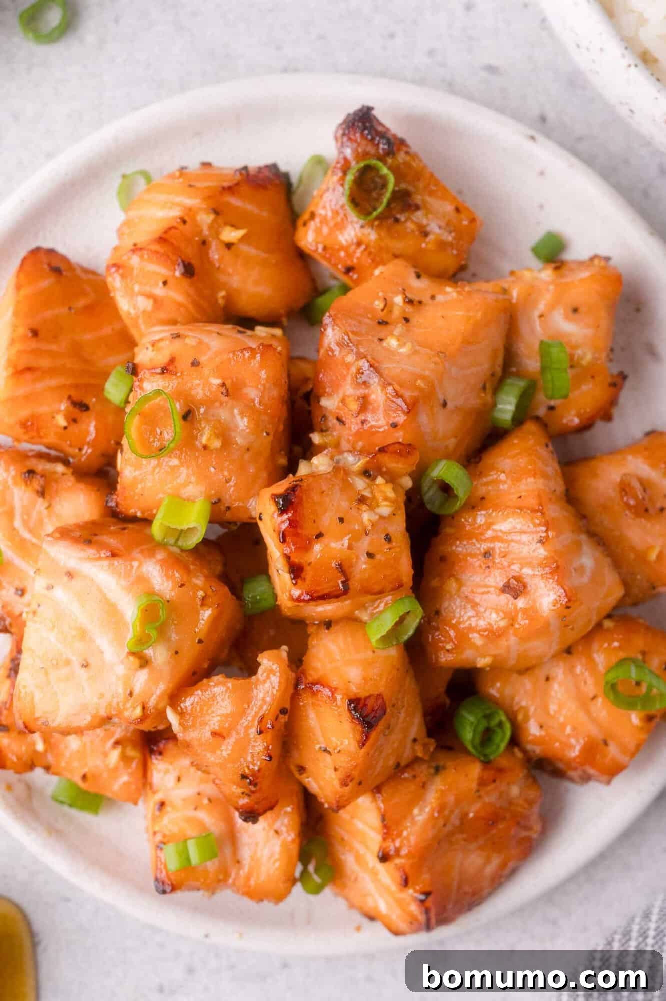 Crispy Honey Garlic Salmon Bites in the Air Fryer 2 A white plate with air fryer salmon bites, garnished with chopped green onions.