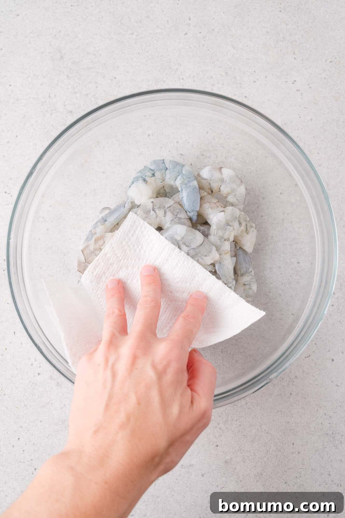 Garlic Butter Shrimp Scampi with Lemon and Parsley 4 Hand patting shrimp dry with a paper towel in a glass bowl.