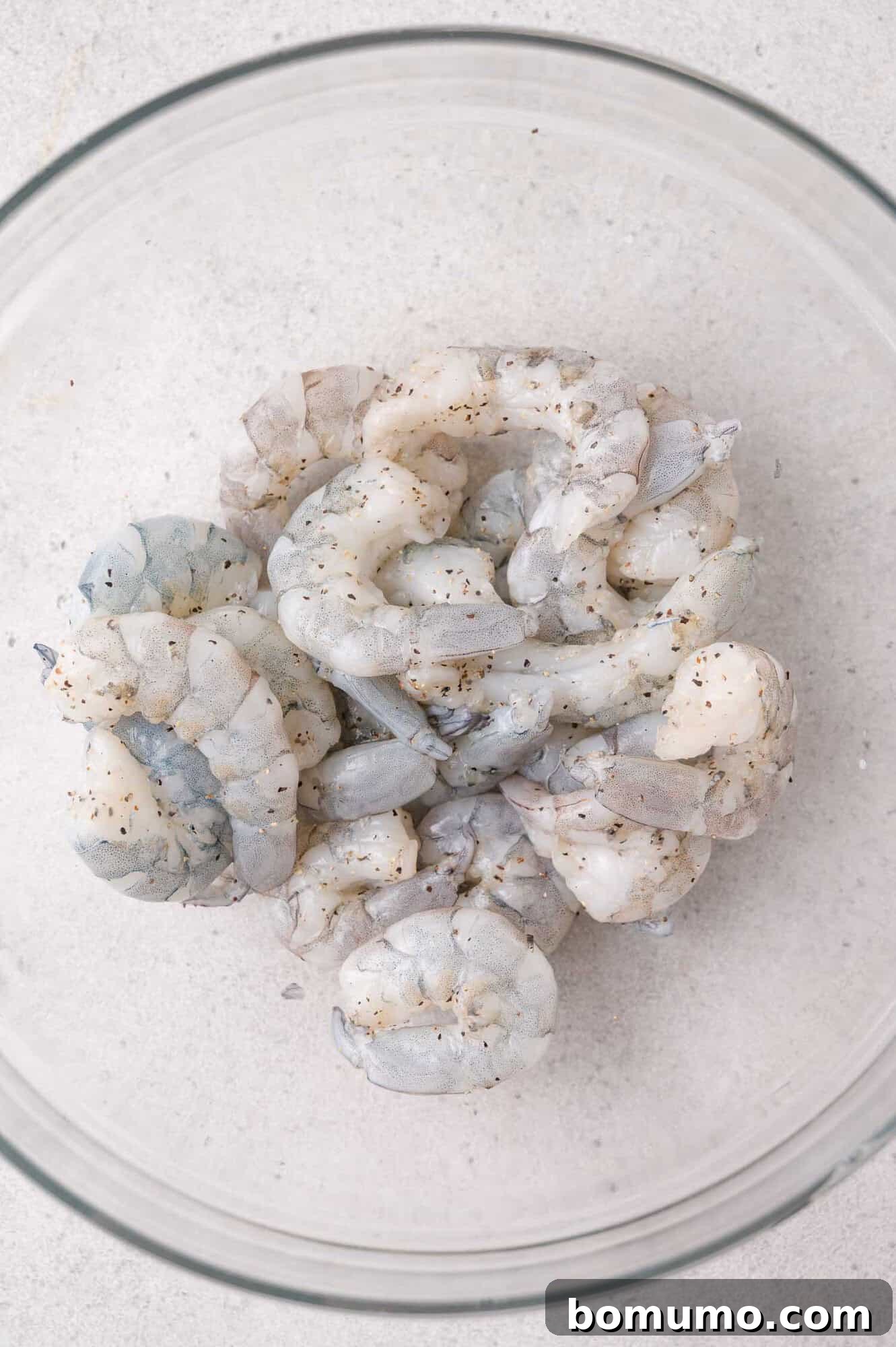 Garlic Butter Shrimp Scampi with Lemon and Parsley 5 Seasoned raw shrimp in a clear bowl with black pepper.