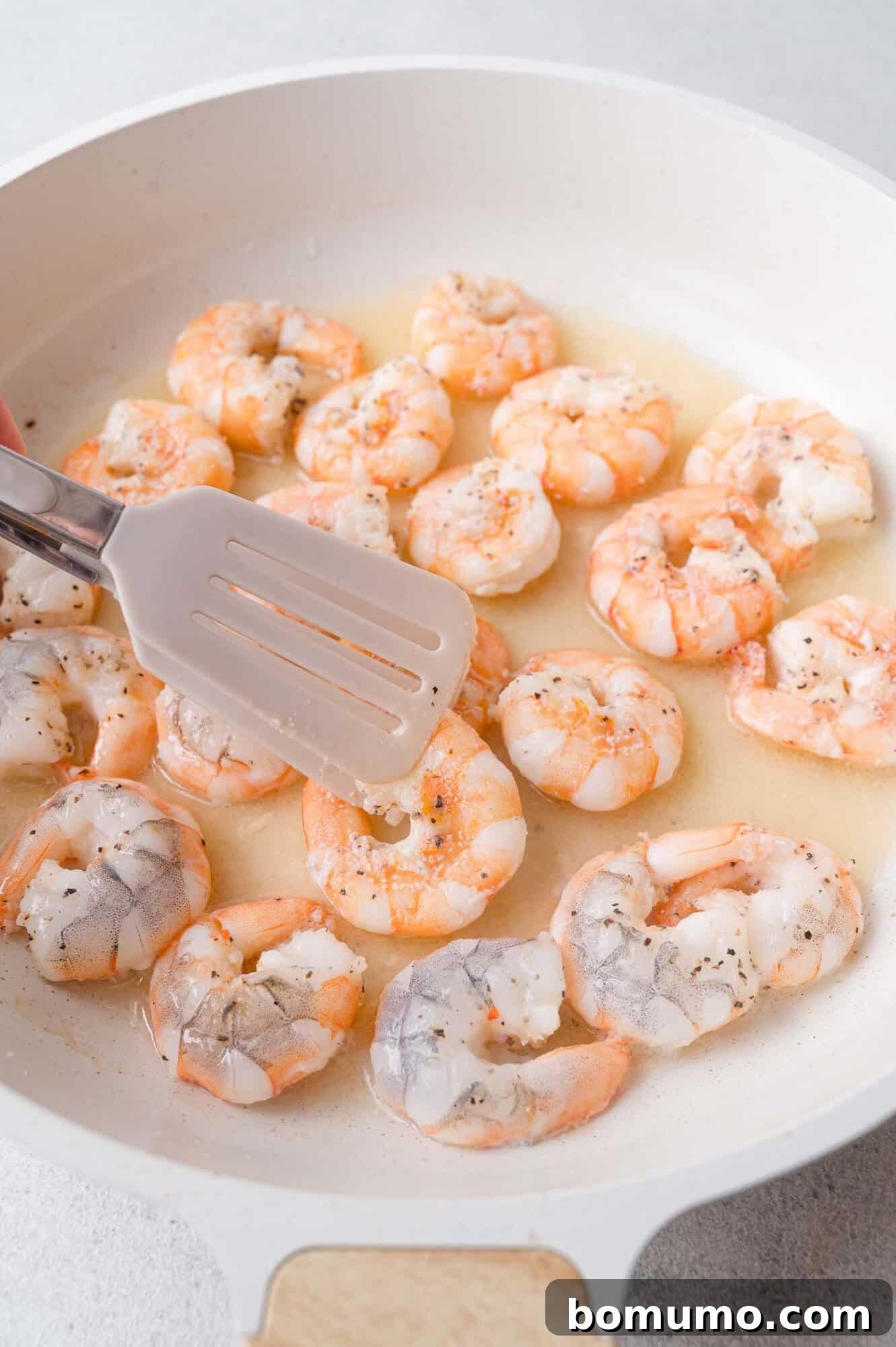 Garlic Butter Shrimp Scampi with Lemon and Parsley 6 A cooked shrimp being held above a skillet with sauce.