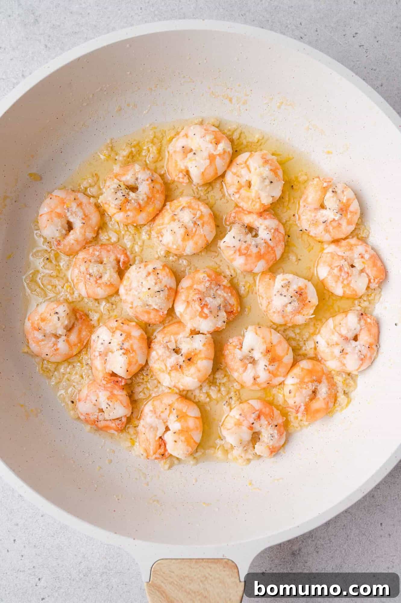 Garlic Butter Shrimp Scampi with Lemon and Parsley 10 Cooked shrimp in a white skillet with garlic butter sauce, topped with herbs.