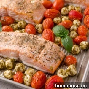 Sheet Pan Caprese Salmon with Tomatoes and Basil 17 Baked salmon fillets on a sheet pan with roasted cherry tomatoes, mozzarella balls with pesto, and fresh basil leaves.