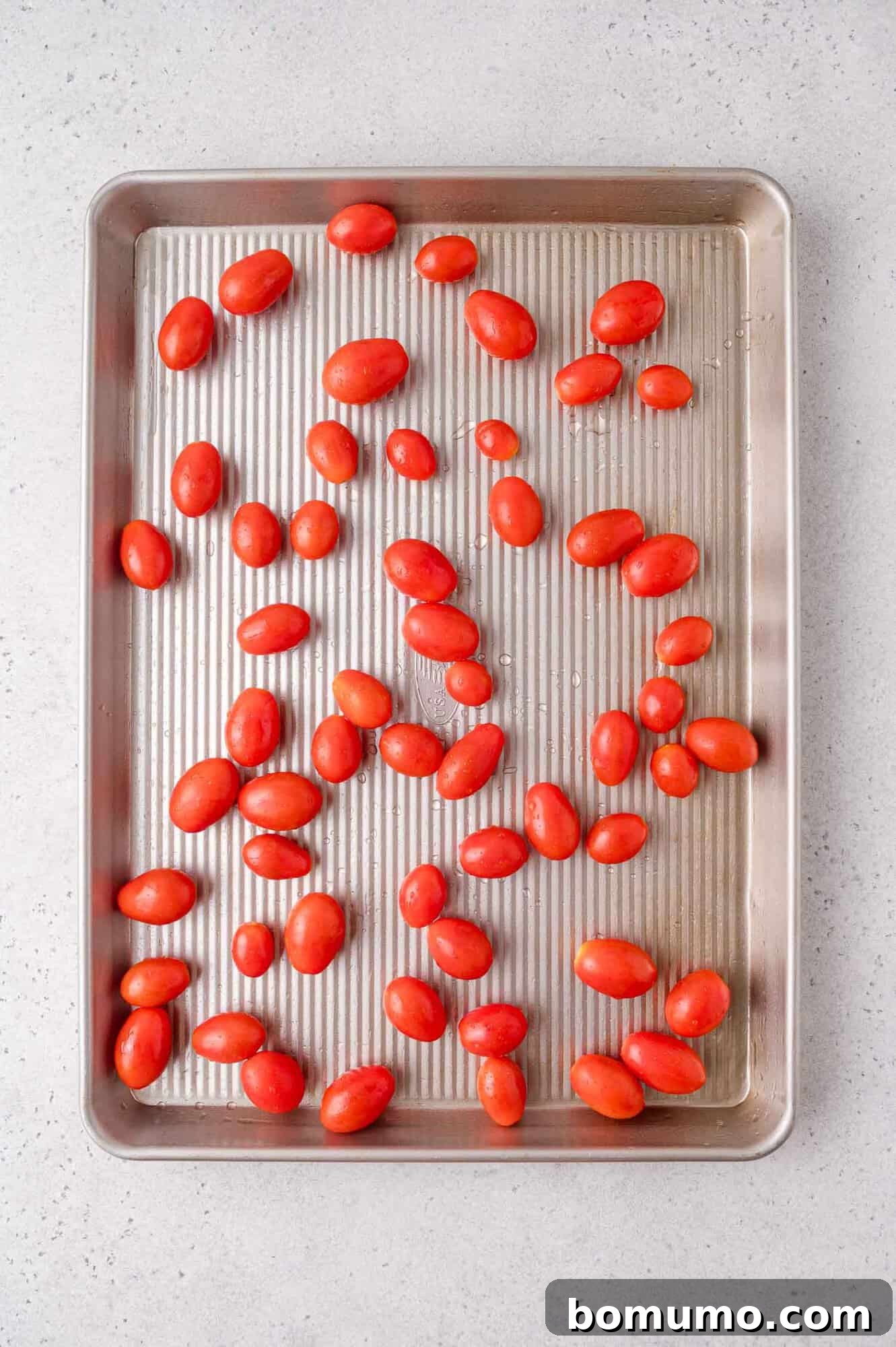 Sheet Pan Caprese Salmon with Tomatoes and Basil 5 A baking sheet with raw grape tomatoes spread out evenly on a light-colored countertop.