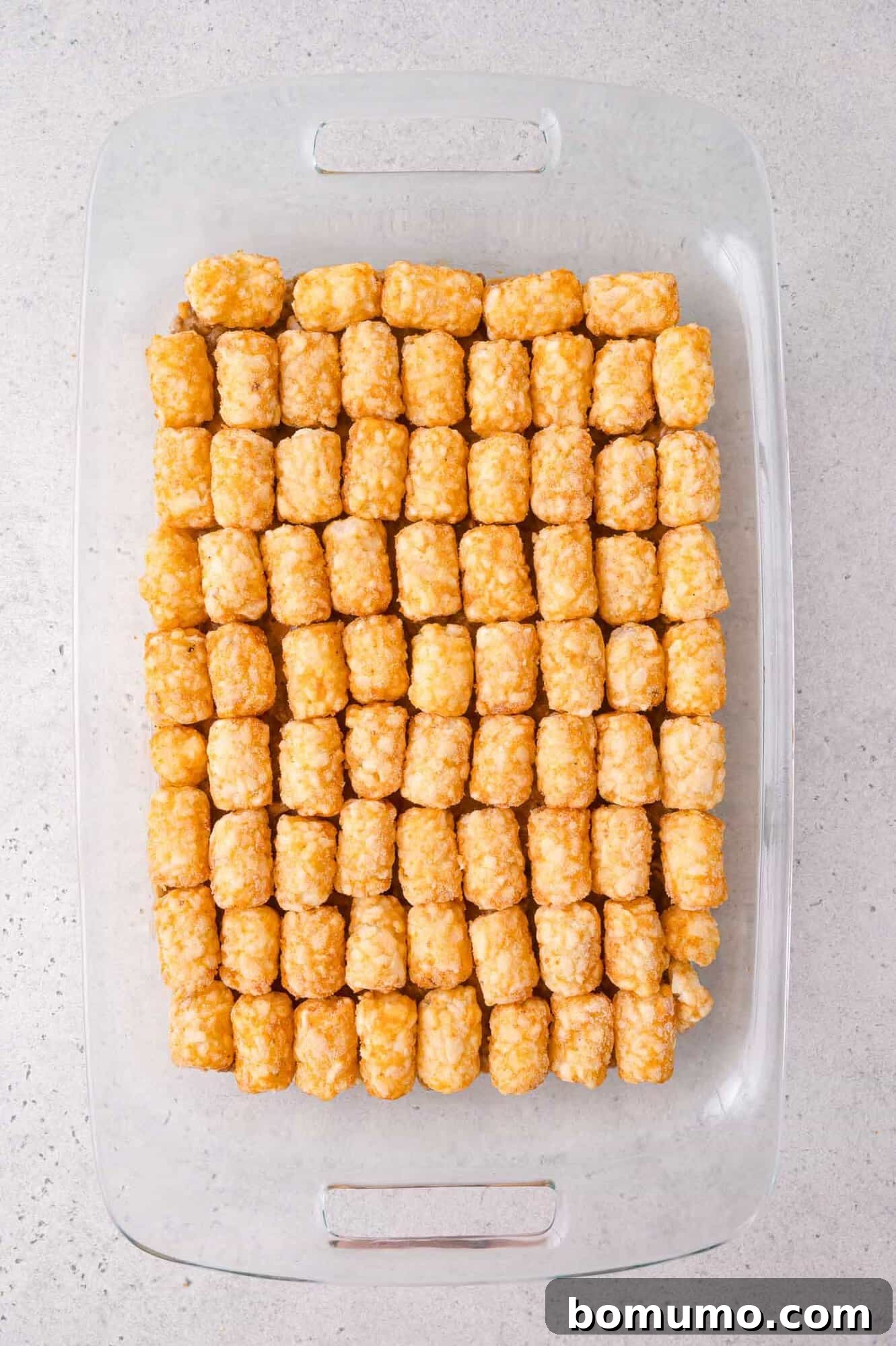Cheeseburger Tater Tot Casserole Made Without Canned Soup 8 A glass baking dish filled with neatly arranged rows of golden tater tots on a light-colored countertop.